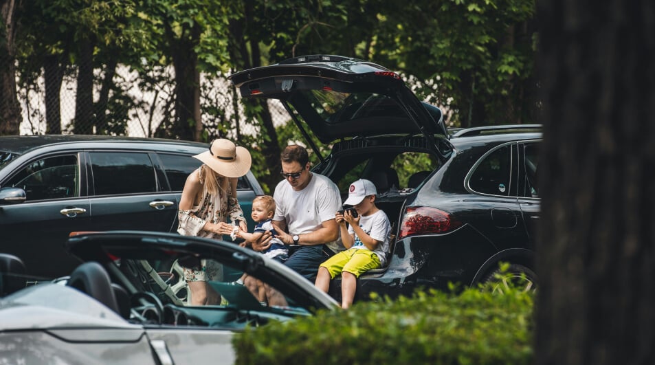 A family sitting at the open boot of their car in a car park