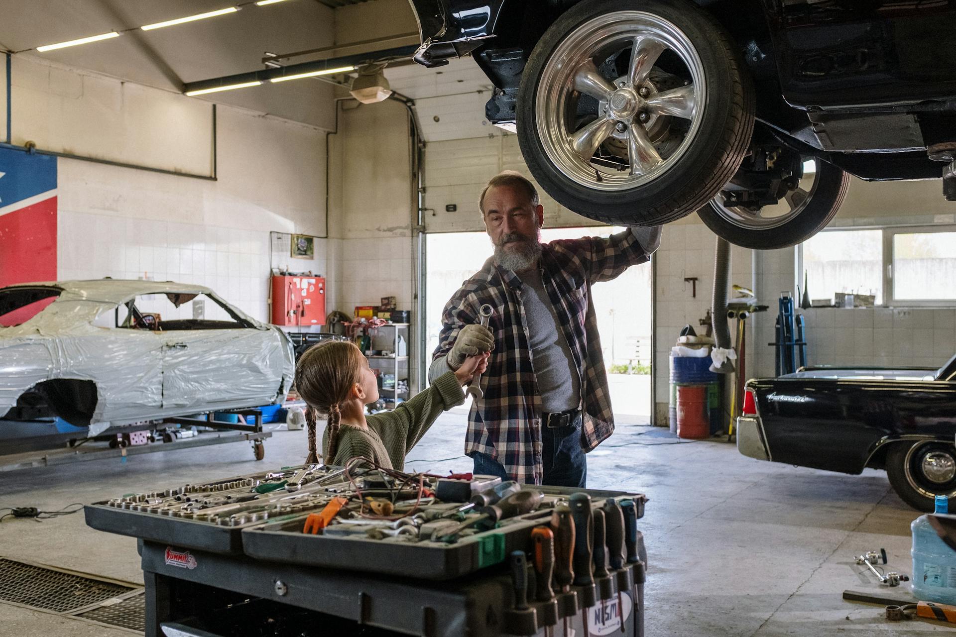 A father and his young daughter working on a car together in a garage