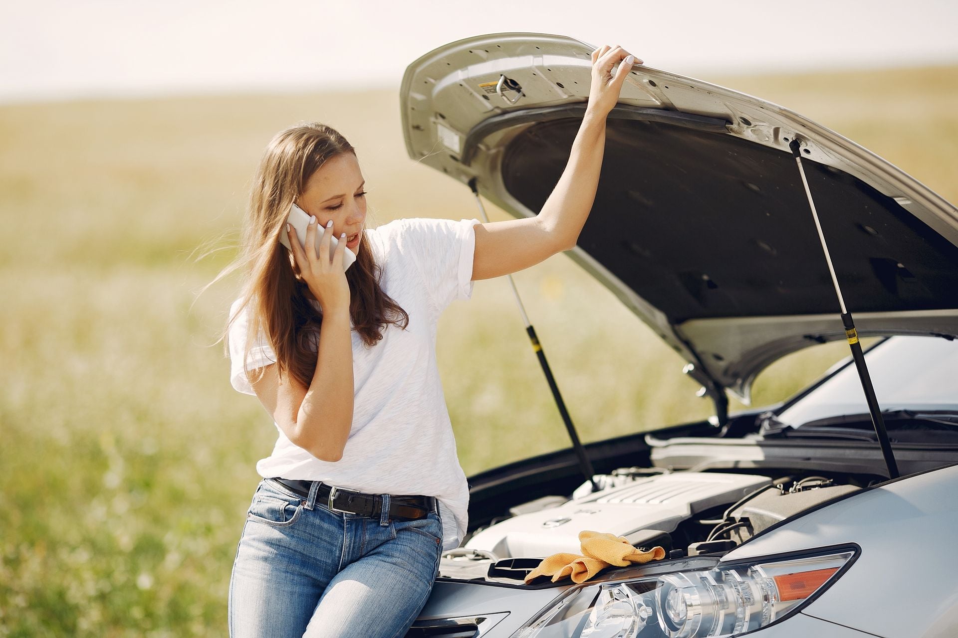 A driver on the phone beside a broken-down car with the bonnet raised