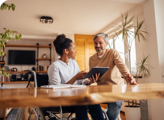 Woman and man at kitchen table looking at tablet and smiling.