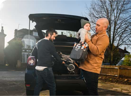 One man holding a baby and bag, whilst another man pulls push chair out of boot.