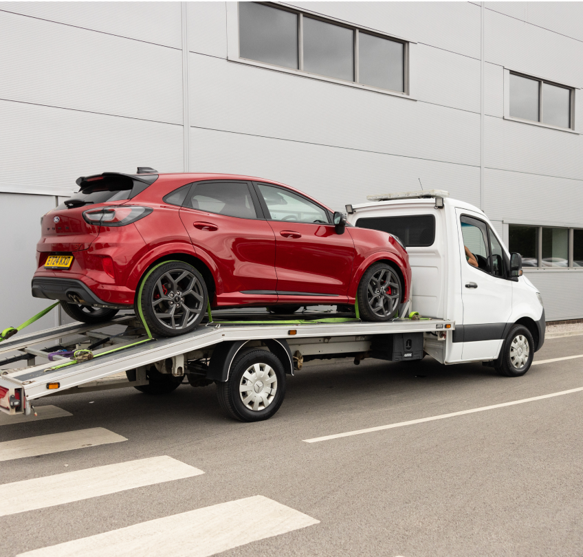 A red car secured on the back of a truck